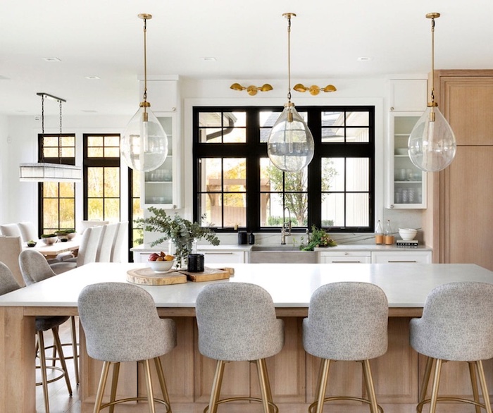  A modern kitchen with a large central island, six bar stools, and three pendant lights showing large series 400 Series windows in black.